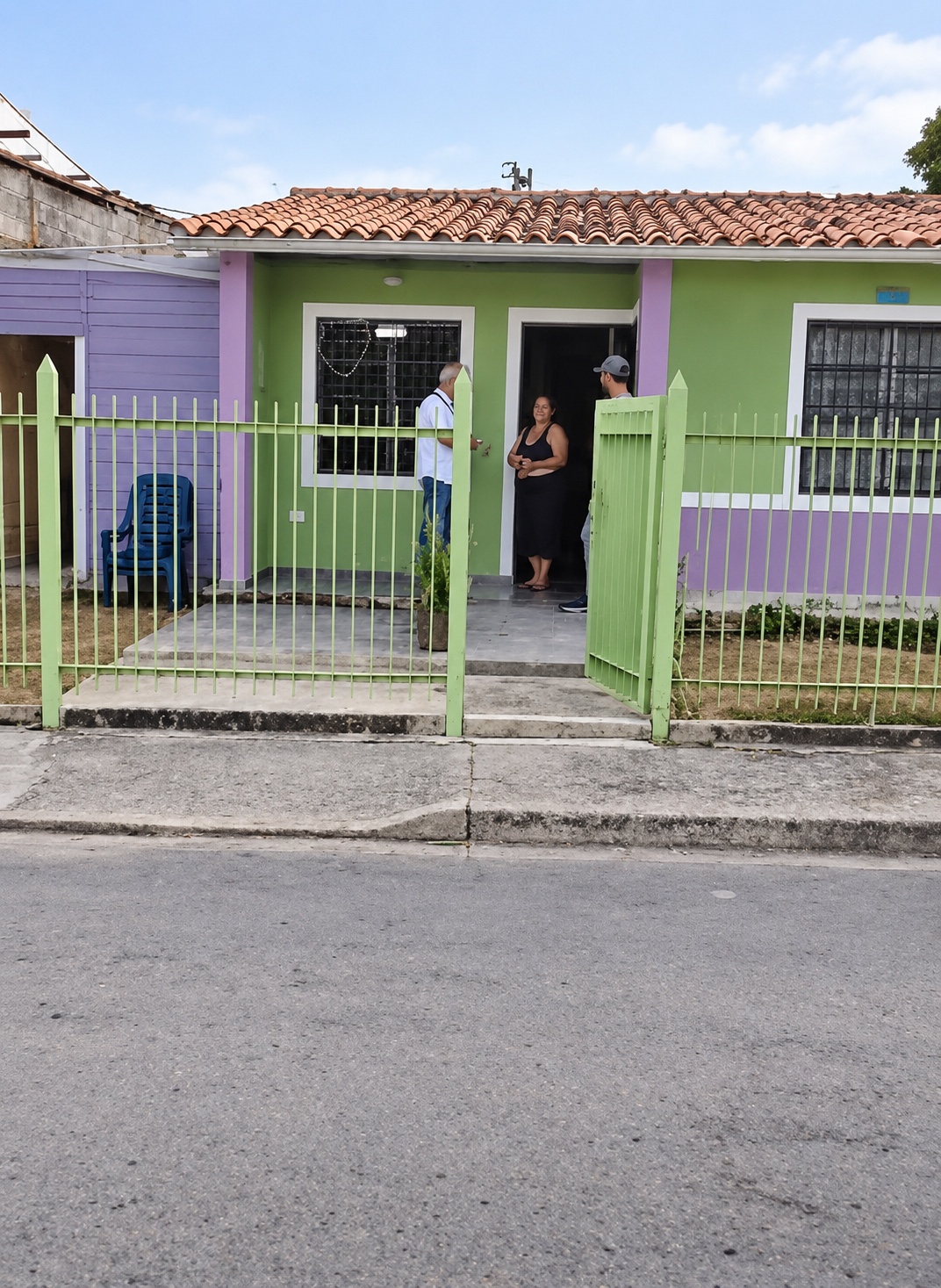 Casa pintada de verde y morado con techo de tejas y reja verde