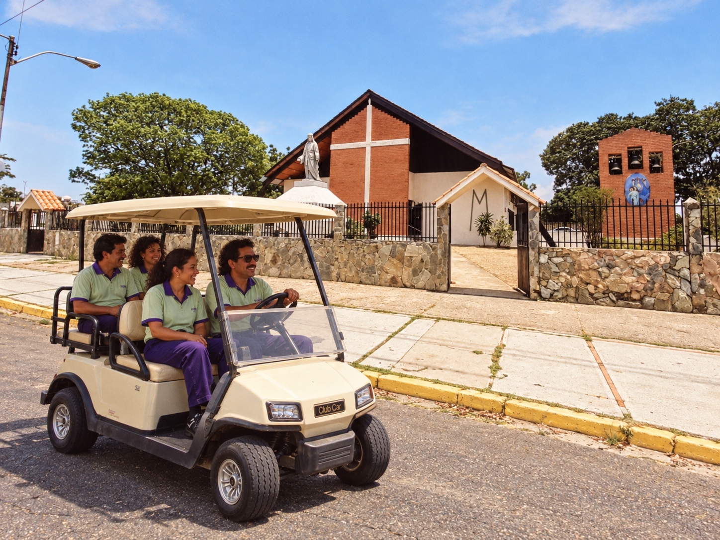 Carrito de golf con vecinos uniformados recorriendo una calle de Ciudad Alianza frente a una iglesia de ladrillo